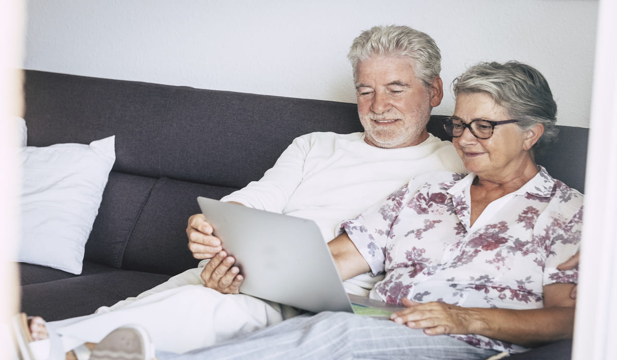una pareja de ancianos usando un portátil en el sofá