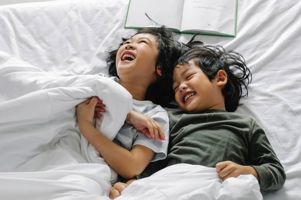 dos niños asiáticos abrazados y riendo en una cama