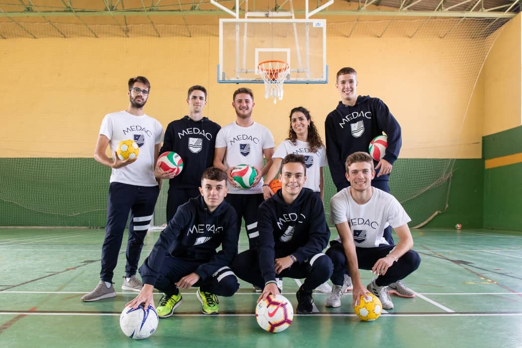 Grupo de alumnos de MEDAC posando como un equipo con balones de diferentes deportes