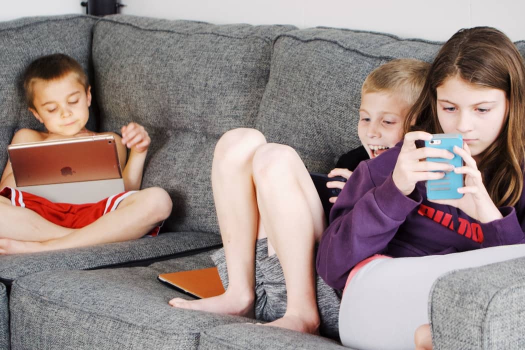 tres niños usando dispositivos digitales en un sofá