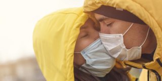 Dos personas con mascarillas y chubasquero amarillo besándose