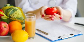 Nutricionista cogiendo un tomate entre sus manos y con frutas encima del escritorio