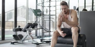 hombre deportista fatigado sentado en una banca del gimnasio