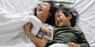dos niños asiáticos abrazados y riendo en una cama
