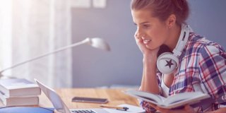 chica joven estudiando en casa con su portátil, apuntes y unos cascos