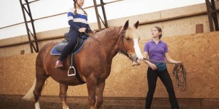 una guía ecuestre enseñando a montar a caballo a una niña
