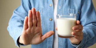 persona intolerante a la lactosa con un vaso de leche en la mano y gesto de rechazo