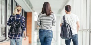 Dos chicas y un chico de espalda andando por un pasillo de instituto