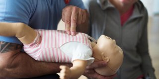 profesional explicando como hacer la rcp en niños presionando con dos dedos el pecho de un muñeco