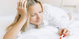 Mujer rubia observando un test de embarazo con cara de frustración sobre su cama