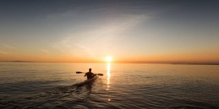 Hombre de espalda con su kayak en el mar mirando el atardecer