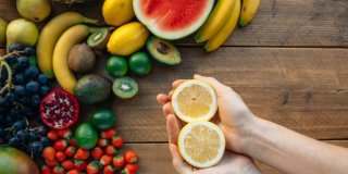 mesa con frutas que contienen vitamina C y una mano sosteniendo las dos mitades de una naranja
