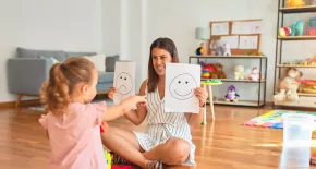 Educadora enseñando dos carteles con caras a una niña para identificar emociones
