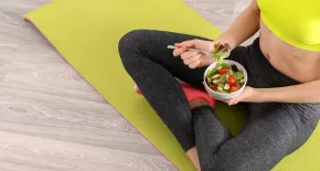 chica deportista sentada en una esterilla comiendo una ensalada