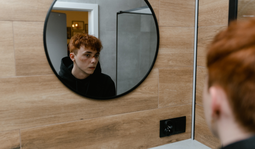 Joven con magulladuras en la cara mirándose al espejo en el baño