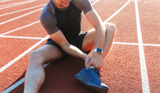 Atleta sentado en una pista de correr presionando su tobillo por un dolor