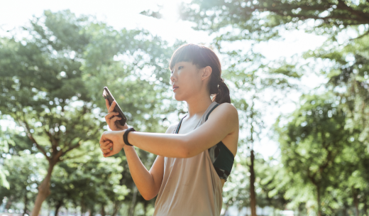 Mujer haciendo deporte en la naturaleza y comprobando su actividad en su teléfono y su pulsera de actividad