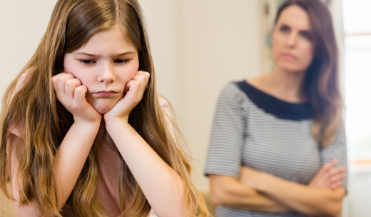 Primer plano de niña enfadada con su madre detrás cruzada de brazos
