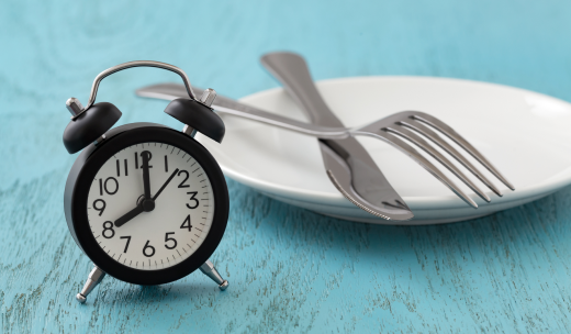 Reloj marcando las ocho y un plato con cubiertos en una madera azul