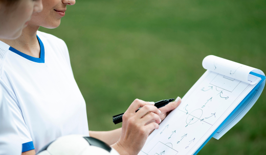 Primer plano de una entrenadora apuntando la jugada en una libreta