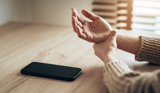Primer plano de las manos de una persona frente a un teléfono sujetándose una muñeca