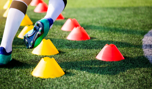 Piernas de un jugador de fútbol esquivando conos de colores en el césped