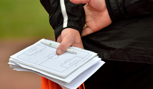 Entrenador con las manos enlazadas detrás de las espalda sujetando una libreta y un bolígrafo