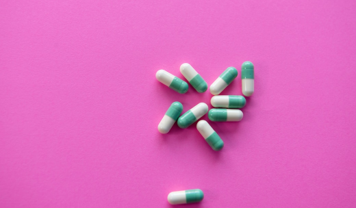 Cápsulas de medicamento blancas y azules sobre una superficie rosa