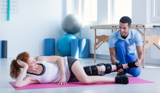 Mujer tumbada en el suelo y con una prótesis en la pierna haciendo ejercicios con la ayuda de un especialista
