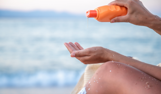 Primer plano de las manos de una persona echándose protector solar en la playa