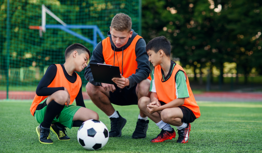 Tres futbolistas infantiles en un campo de fútbol viendo las jugadas en una carpeta