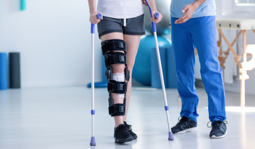 Una persona con prótesis en la rodilla andando con muletas al lado de un especialista