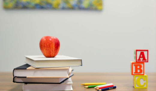 Libros con una manzana arriba, lápices y cubos de letras encima de una mesa