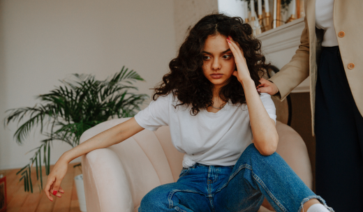 Chica joven sentada en un sillón con actitud reflexiva con la mano en la cabeza