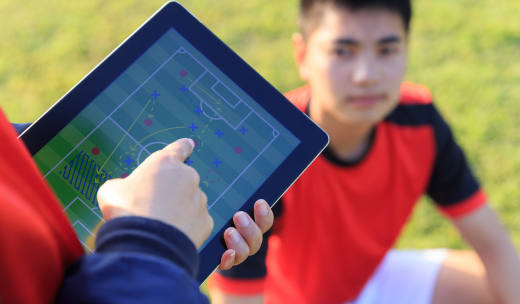 Entrenador explicando una jugada en su tablet a un niño futbolista en el campo