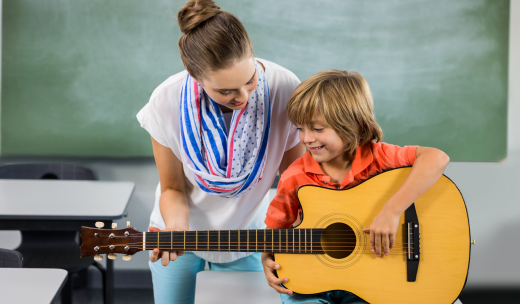 Profesora enseñando a un niño rubio tocar la guitarra en un aula