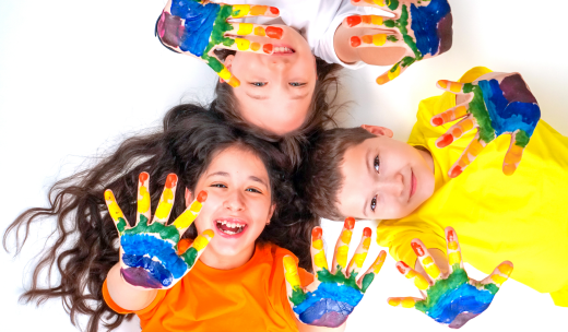 Dos niñas y un niño sonriente con las palmas de las manos pintadas hacia arriba