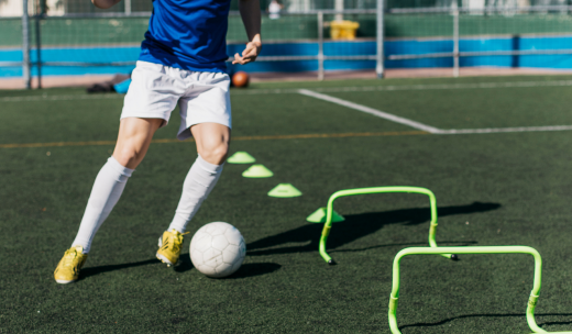 Primer plano de unas piernas de futbolistas saltando obstáculos en un campo de fútbol con un balón