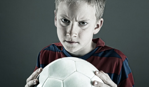 Cara de un niño enfadado con un balón de fútbol entre sus manos
