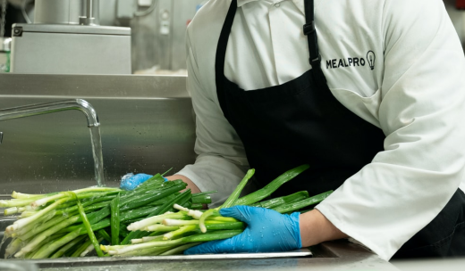 Un cocinero con guantes lavando verduras en el grifo del fregadero