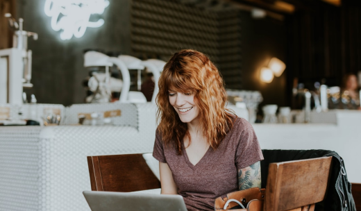 Mujer pelirroja sonriente mirando su ordenador en una cafetería