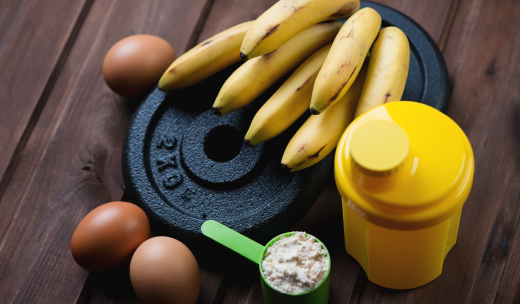 Primer plano de frutas y alimentos proteicos alrededor de unos discos de pesas