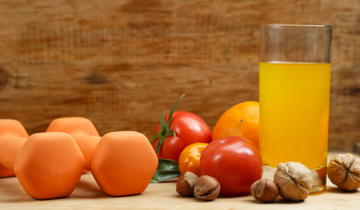 Bodegón de frutas y verduras en tonos cálidos junto a unas mancuernas naranjas