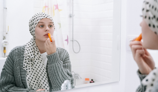 Mujer con cáncer con un pañuelo en la cabeza pintándose los labios en un baño