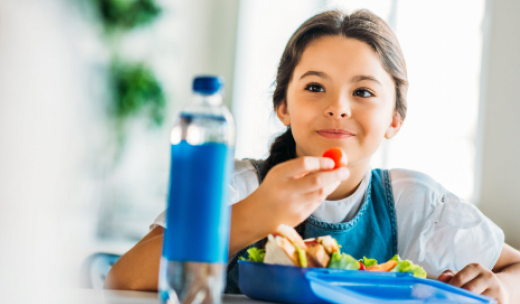 Niña asiática sentada en una mesa comiendo ensalada y cogiendo un tomate cherry entre sus dedos