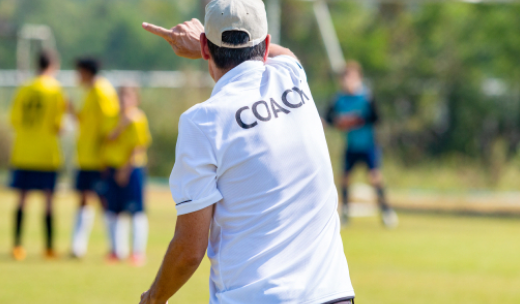 Primer plano de un entrenador de fútbol de espalda dando indicaciones a los jugadores