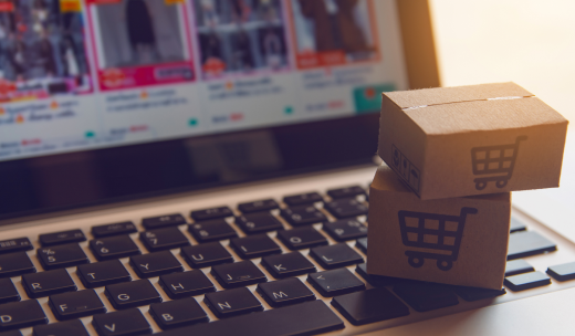 Cajitas de cartón con el icono del carrito de la compra encima de un portátil con un ecommerce en la pantalla