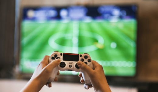 Mando de videoconsola delante de una pantalla con juego de fútbol