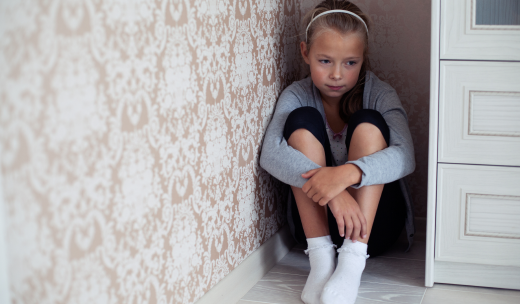 Niña escondida detrás de un mueble con actitud asustada
