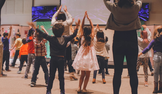 Un grupo de niños pequeños de espalda bailando en una sala junto a sus profesoras
